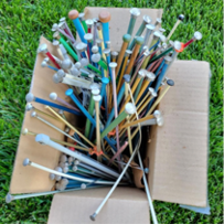 A cardboard box full of multi-colored, mismatched knitting needles