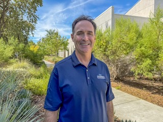 Granger standing outside. Plants, a walkway, and a building are in the background.